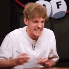 a man in a white shirt is making a funny face in front of a sign with the letter f on it