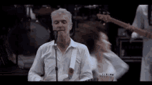 a man in a white shirt is singing into a microphone while playing a guitar