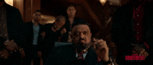 a man in a suit and tie is sitting in front of a group of men with the word brothers on the bottom right