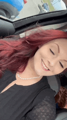 a woman with red hair and a pearl necklace is smiling in a car