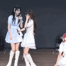 a girl with a flower in her hair holds a microphone while another girl looks on