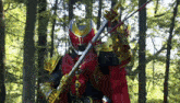 a person in a red and gold costume is holding a sword in a forest .