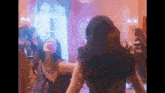 two women are dancing in front of a mirror in a room . one of the women is wearing a black dress .