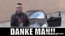 a man in a leather jacket and sunglasses is standing in front of a black car with the words danke man written above him .