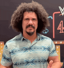 a man with curly hair and a beard stands in front of a chalkboard with the number four on it