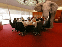 a group of people are sitting around a table with an elephant in the middle