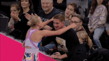 a man in a hilfiger shirt applauds while a woman hugs him