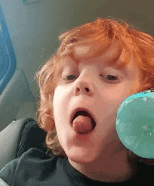 a young boy with red hair is blowing a bubble with his tongue
