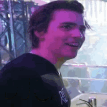 a man in a black shirt is smiling in a dark room with purple lights behind him .