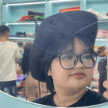 a girl wearing glasses and a hat looks at herself in a mirror