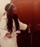 a woman in a white robe is standing in front of a door and screaming .