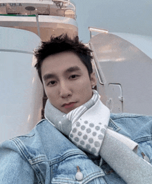 a man wearing a denim jacket and a scarf is taking a selfie