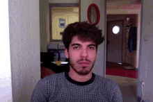 a man with a beard wearing a black and white checkered shirt looks at the camera