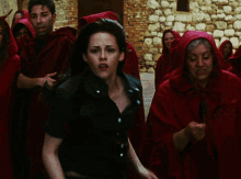 a woman in a green shirt stands in front of a group of people wearing red hoods