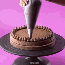 a person is frosting a chocolate cake on a cake stand that says mr.cakes on it