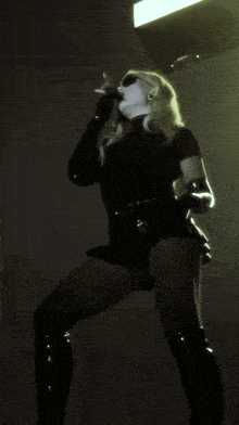 a woman in a black outfit is smoking a cigarette in a dark room