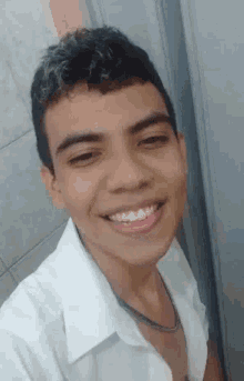 a young man in a white shirt is smiling and taking a selfie