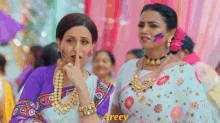 two women are standing next to each other in a crowd and one of them is covering her mouth with her hand .