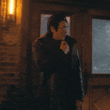 a man in a black coat and glasses stands in front of a glass door