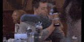 a man and a woman hugging in a restaurant with abc written on the bottom left