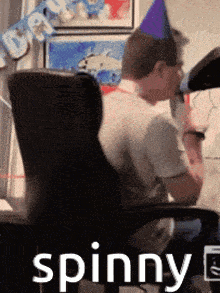 a man wearing a party hat is sitting in a chair with the word spinny written on the bottom .