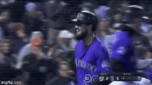 a baseball player wearing a purple uniform is standing in the dugout during a game .