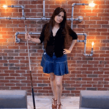 a woman in a denim skirt is holding a pool cue in front of a brick wall