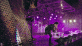 a man singing into a microphone on a stage with purple lights and the letter d in the corner