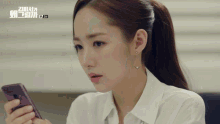 a woman in a white shirt is looking at her phone with a foreign language on the bottom right