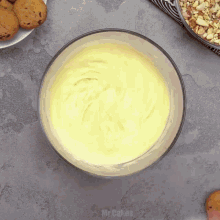 a bowl of yellow frosting is on a table next to a plate of cookies