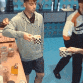 a man in a grey hoodie pours something into a checkered cup
