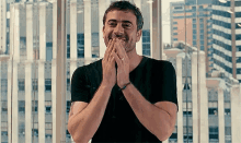 a man in a black shirt is smiling with his hands on his mouth