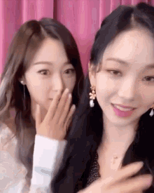 two young women are sitting next to each other and one is covering her mouth with her hand .