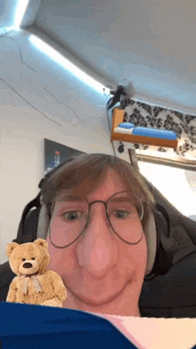 a man wearing glasses and headphones holds a teddy bear in front of his face .