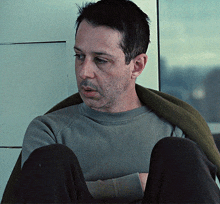 a man wearing a grey sweater and black pants is sitting down