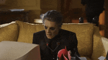 a man in a black suit is sitting on a couch looking at a computer monitor .