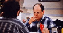 two men are sitting at a table eating food and one is holding a ketchup dispenser .