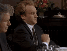 a man in a suit and tie is sitting at a table with other men .