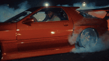 a man is driving a red car with a sticker on the door that says ' toyota ' on it