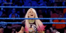 a woman is standing in a wrestling ring with a crowd behind her and screaming .