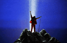 a man in a red suit is standing on top of a rocky hill with his arms in the air