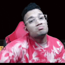 a man wearing glasses and a pink shirt is sitting in a chair .