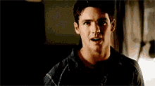 a man in a black shirt is standing in a dark room looking at the camera .