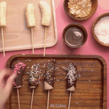 a wooden tray with bananas dipped in chocolate and sprinkles says mr.cakes