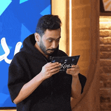 a man in a black hoodie is holding a piece of paper that says ' ao ' on it
