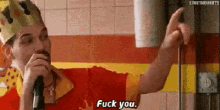 a man in a king 's crown is holding a microphone and saying `` fuck you '' in a restaurant .