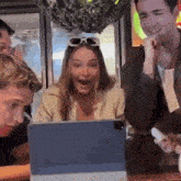 a group of people are sitting around a table looking at a laptop .