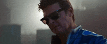 a man wearing sunglasses and a blue jacket is standing in front of a microphone .