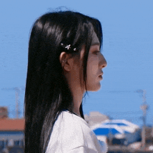 a close up of a woman 's face with long black hair and a blue sky in the background .