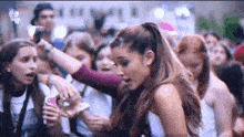 a woman in a ponytail stands in a crowd of people looking at her phone